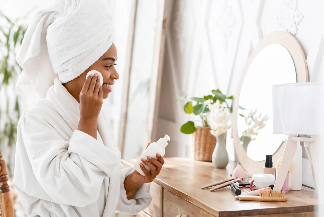 روتين العناية بالبشرة للمرأة السعودية العاملة | دليل شامل 2025 3 black woman cleaning face with cleansing milk and 2025 03 18 18 47 21 utc